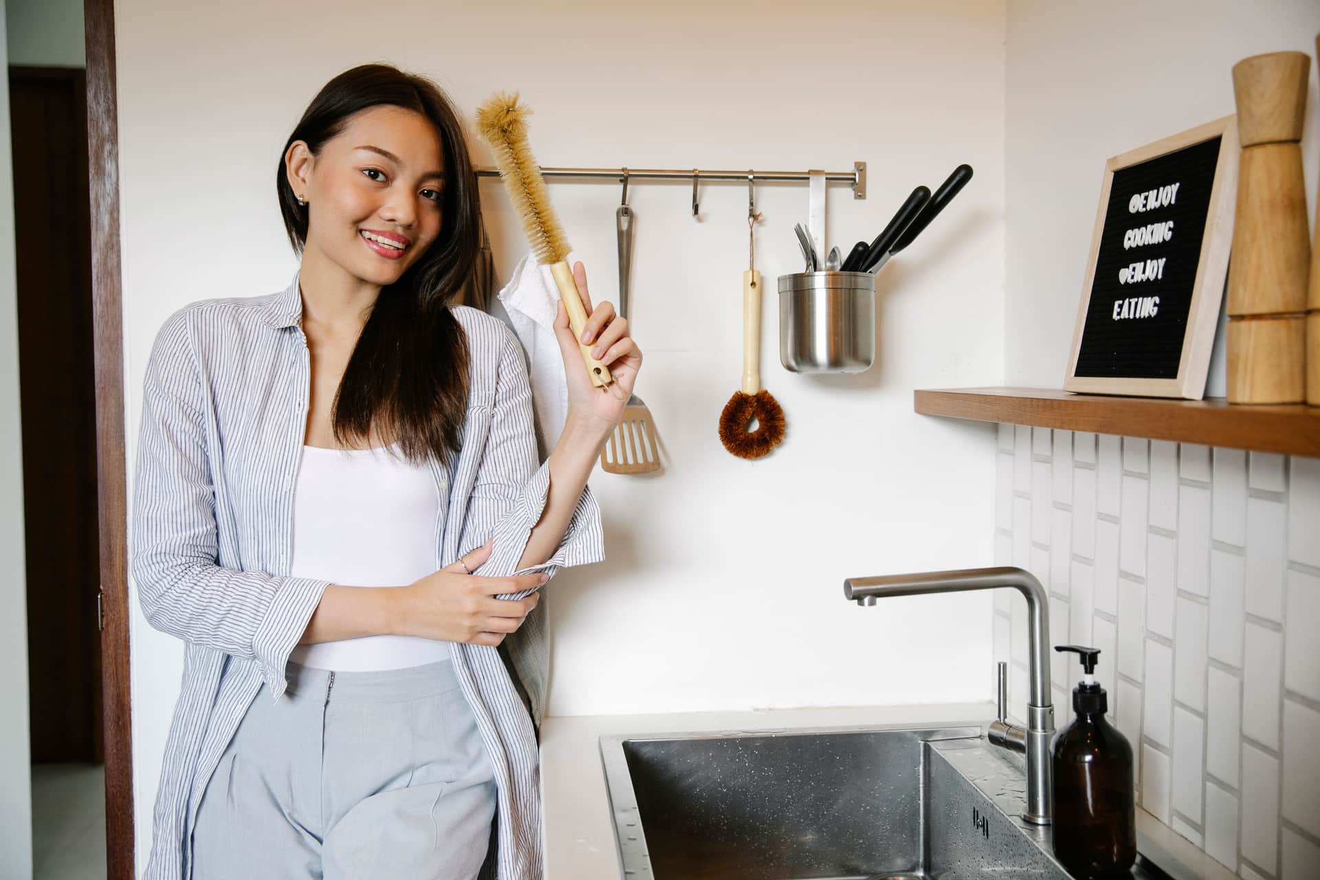 A cleaning brush, cloth and bottle beside a sink